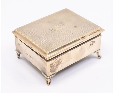 A George V silver engine turned raised cigarette box, plain body on four scroll feet, the cover engraved initials: WAB, fitte