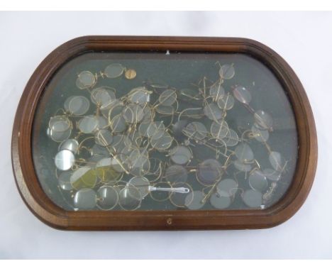 A quantity of vintage and antique spectacles of various forms in oval glazed wooden display case