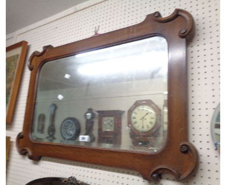 A 20th Century oak framed mirror bevelled wall mirror with decorative C-scroll corners and rounded oblong plate