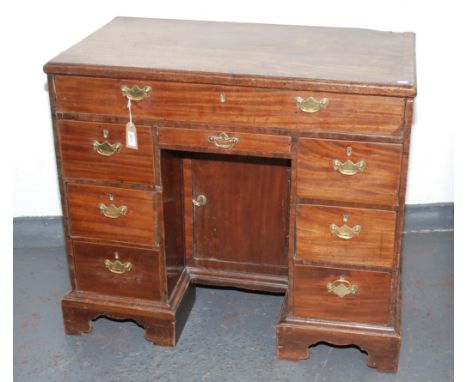 A George III mahogany kneehole desk, the rectangular moulded top above a central cupboard door flanked by an arrangement of e