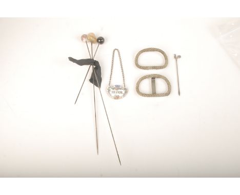 Three hat pins, a silver cocktail stick, a brandy decanter label and a pair of heavy silver buckles. 