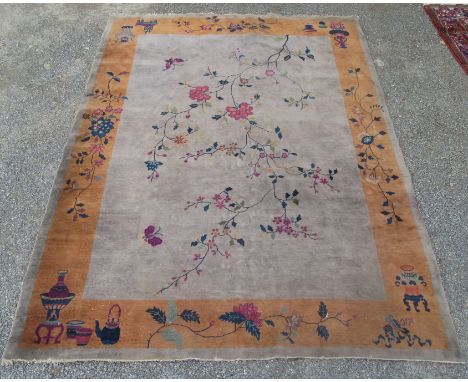 An Art Deco Chinese carpet, the grey field with a flowering tree within a saffron border decorated with vases, other artefact