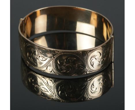 A 9ct rolled gold bangle featuring engraved decoration to one half. Makers mark 'W.P' to inside.  Safety chain is missing.