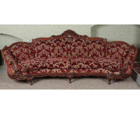 A very large carved mahogany sofa with red floral upholstery. Length 280cm.  Some tears to upholstery.