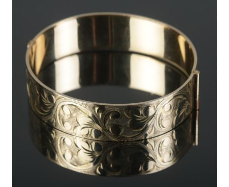 A 9ct rolled gold bangle featuring engraved scroll decoration to one half.  