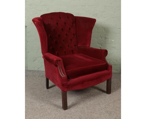 A wing back arm chair with button back and red velvet upholstery.  