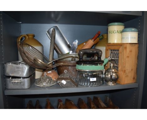 A shelf full of vintage and antique kitchenalia, including enamel storage tins, stoneware flagon, mess tins and an ice shaver