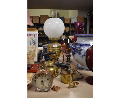 A early 20th century brass oil lamp with opaque shade, a brass blow torch, kettle, stove and copper Puritan alarm clock dated