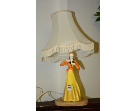 An Art Deco glazed pottery figural table lamp, in the form of a female with orange jacket and yellow skirt, raised on onyx ba