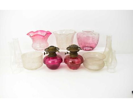 Two 19th century cranberry glass paraffin lamps, height 20cm, and five paraffin lamp glass shades, all with etched decoration