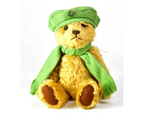 STEIFF; a golden bear wearing green scarf and bonnet with shamrock brooch, with growler, gold button and tag to ear, height 3
