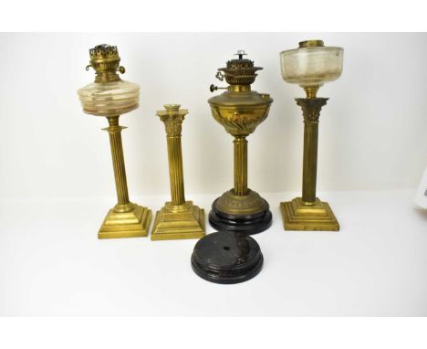 Four brass column paraffin lamps and lamp parts, comprising two with glass fonts, one with brass font, one base and a black m