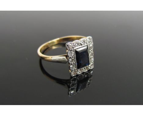 An Art Deco gold sapphire and diamond ring, the central emerald cut blue sapphire framed by diamonds, shank unmarked. Size M,