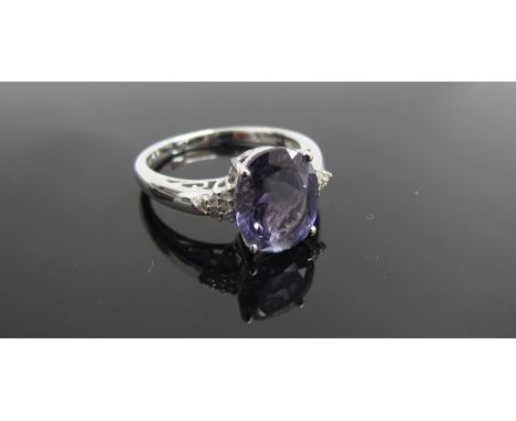 A 9ct white gold ring with oval purple stone flanked by diamond set shoulders. Size R, 3.9g  