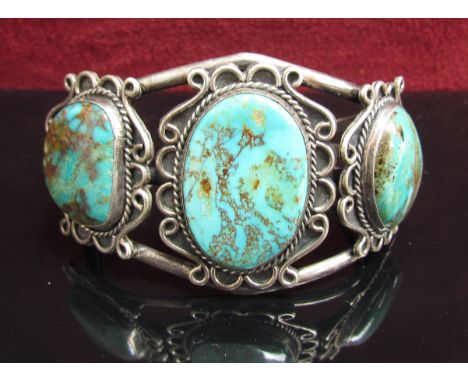 A white metal bangle set with three oval turquoise in scroll mount