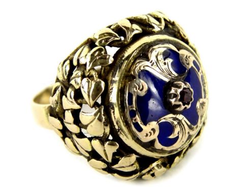 An 18ct gold enamel designed dress ring, with central circular design centre with ruby set stone, and scroll border design, w