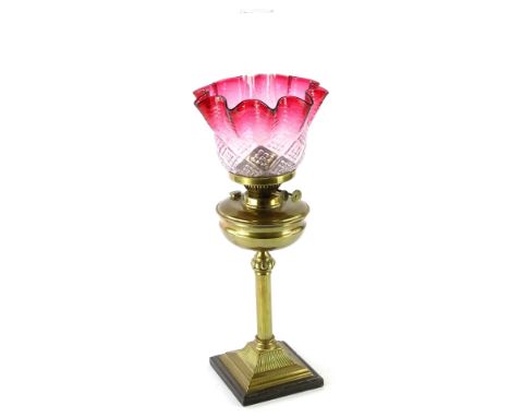 A Victorian brass oil lamp, with cranberry tinted moulded glass shade, the base with reeded column and wooden plinth, 60cm H 