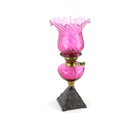 A Victorian and later cranberry tinted table lamp, with petallated and writhern shade, cranberry reservoir and cast iron pier