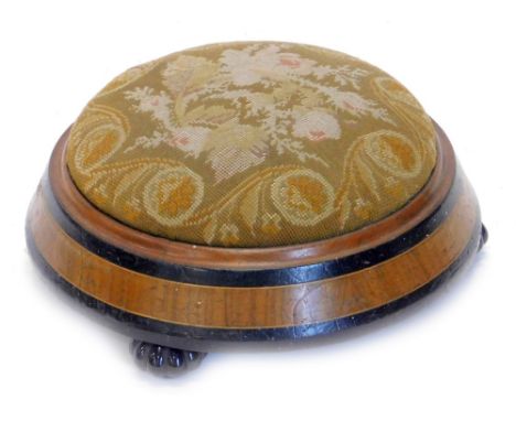 A Victorian ebonised and walnut circular foot stool, with woolwork seat, on lobed black ceramic feet, 31cm dia.