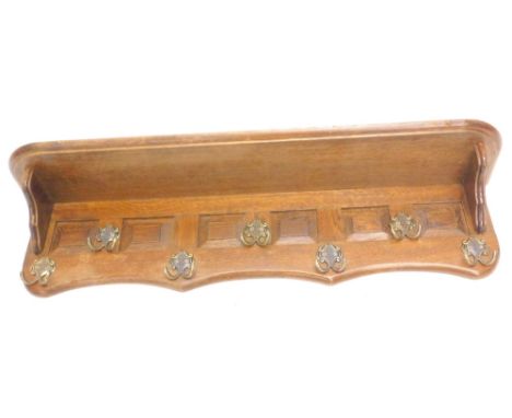 A Continental oak wall mounted coat rack, with panelled front and six gilt metal hooks below a shelf, 100cm W.