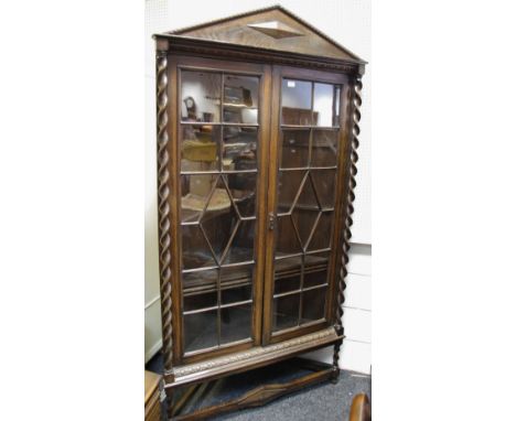 An oak floor standing corner cabinet, architectural pediment, two astragal glazed doors flanked by barleytwist columns. barle