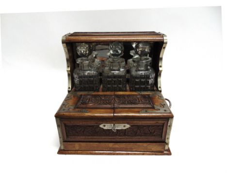 A LATE VICTORIAN / EDWARDIAN OAK TANTALUS  fitted with three decanters, pair of hinged doors opening to compartment for glass
