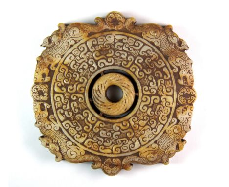 A Chinese Warring States style carved mixed colour jade circular amulet, with roaming dragon surrounding a central pierced ro