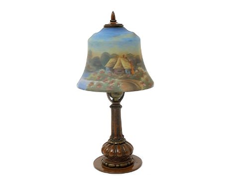 A Miller patinated metal table lamp and reverse painted glass shade, the bell shaped shade painted with thatched cottages on 