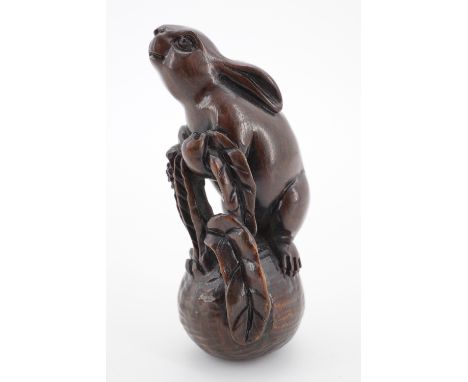 A Japanese carved wooden netsuke modelled as a rabbit tugging on a root vegetable, the rabbit having inset glass eyes, 6 cm