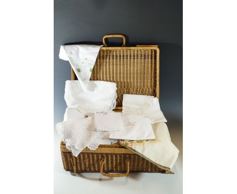 A vintage wicker hamper containing a quantity of vintage linens, including hand embroidered table cloths