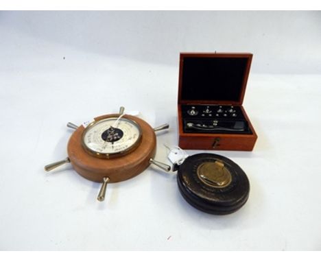 Modern barometer in the shape of a ship's wheel, a leather-bound surveyors measuring tape, a folding rule and a set of weight