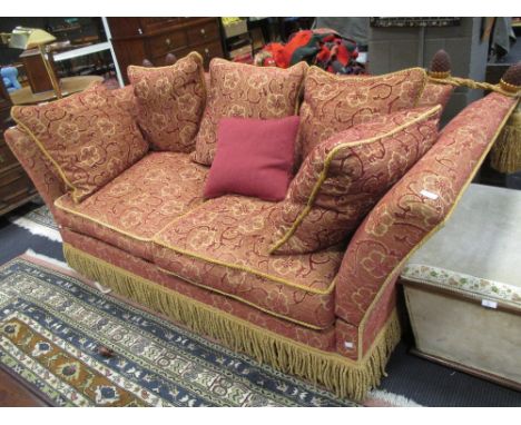 A two seater Knole sofa with pine cone finials upholstered in red and gold fabric with bullion tassel fringe  