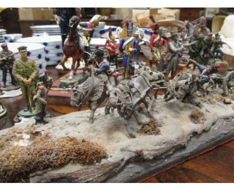 A collection of painted metal model soldiers, depicting various periods, some on stands, a small model canon, and a larger ce