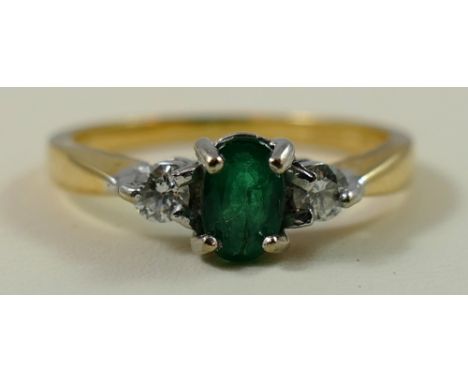 An 18ct gold emerald and diamond three stone ring, claw set with an oval stone flanked by brilliant's, size O.