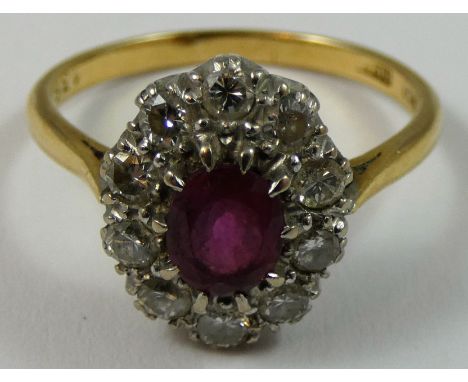 An 18ct gold ruby and diamond oval cluster ring, claw set with a mixed cut stone bordered by ten brilliants of approximately 