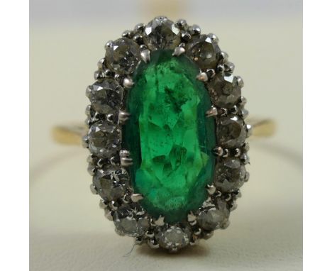 A gold, emerald and diamond oval cluster ring, claw set with a mixed cut stone, measuring 12 x 6 mm, bordered by twelve old c