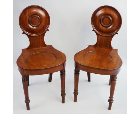 A pair of 19th century mahogany hall chairs, each with moulded edged circular back, shaped seat with dished centre and ring t