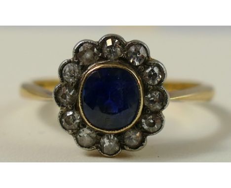 An 18ct gold sapphire and diamond cluster ring, milligrain collet set with an oval mixed cut stone, bordered by twelve old cu