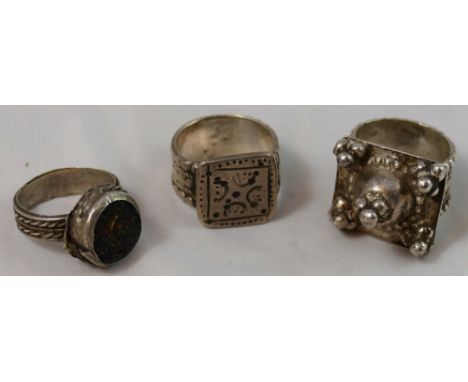 An Omani silver Zar ring, the square base with bead decoration, a silver ring set with a carved red glass disc engraved with 