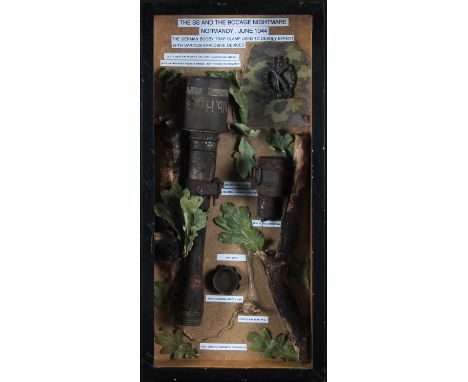 A small framed and glazed display case containing WW2 relics from Normandy to include SS stick grenade, Nazi infantry badge, 