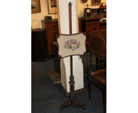 A mahogany adjustable fire screen with floral woolwork panel, on baluster carved stem and raised platform base, on scroll car