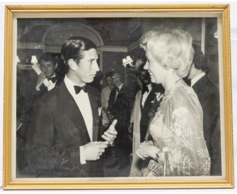 An early 1970s black and white photograph of Joan Morecambe speaking with HM King Charles III when HRH The Prince of Wales, f