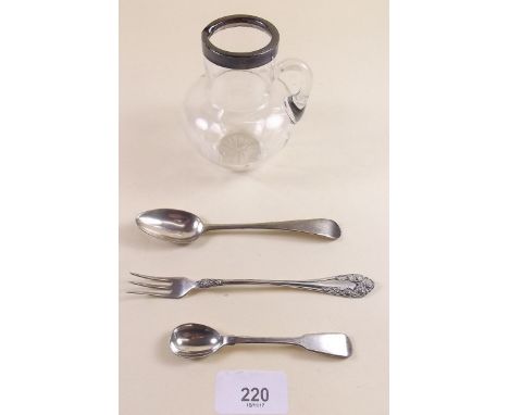 A silver rimmed small glass jug, a pickle fork, mustard spoon and teaspoon