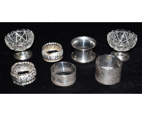 FIVE ASSORTED SILVER NAPKIN RINGS  Weighing a total of approx. 96.4 grams; together with a pair of small round cut glass salt