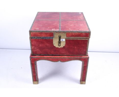 An Eastern red leather trunk on a stand. The exterior with studded details, H61cm x W53cm x D53cm