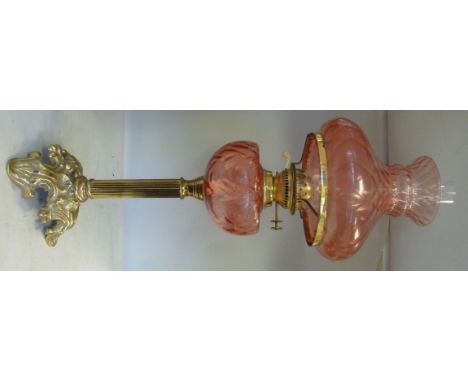 A late 19thC/early 20thC oil lamp, the burner set on a Cranberry coloured glass reservoir, a reed moulded column and a decora