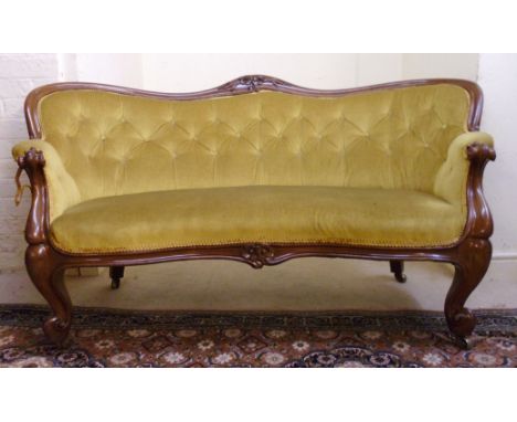 A late Victorian mahogany showwood framed settee, having a floral carved, arched, curved back and scrolled arms, part button 
