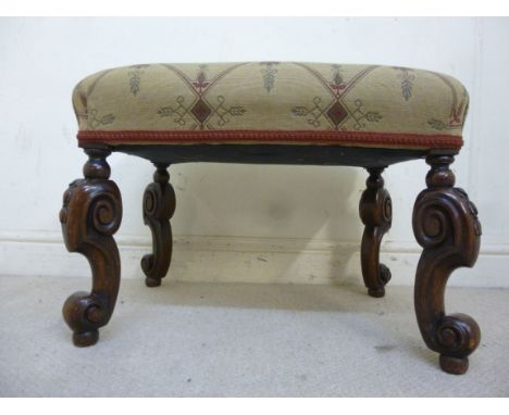 A 1920s walnut framed stool, having a tapestry style fabric upholstered top, raised on scrolled legs with foliate carved knee