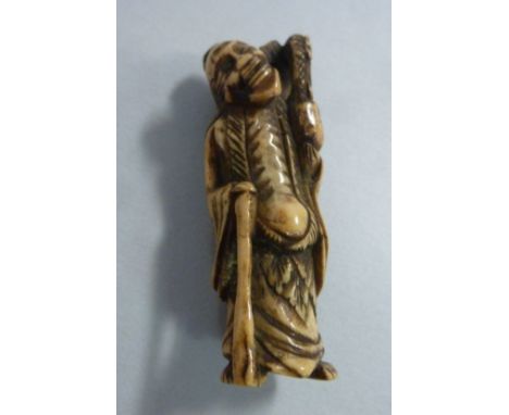 A late 19th/early 20thC carved ivory netsuke, a standing allegorical figure with a staff, a dragon climbing on his shoulders