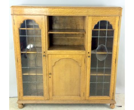 An oak lead glazed 2 door bookcase cupboard with adjustable shelves on bun feet. 125 x 120 x 30cm